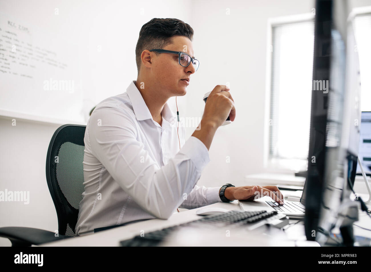 Lächelnd Software Entwickler sitzt in seinem Büro Schreibtisch arbeiten am Laptop das Tragen von Kopfhörern. Mann mit Brille arbeiten am Laptop im Büro Stockfoto