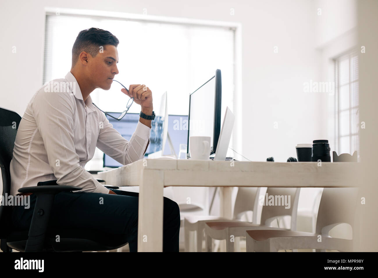 Software Entwickler sitzt in seinem Büro Schreibtisch bei Laptop schauen und denken mit Brille im Mund. Mann mit Brille arbeiten an Comp Stockfoto