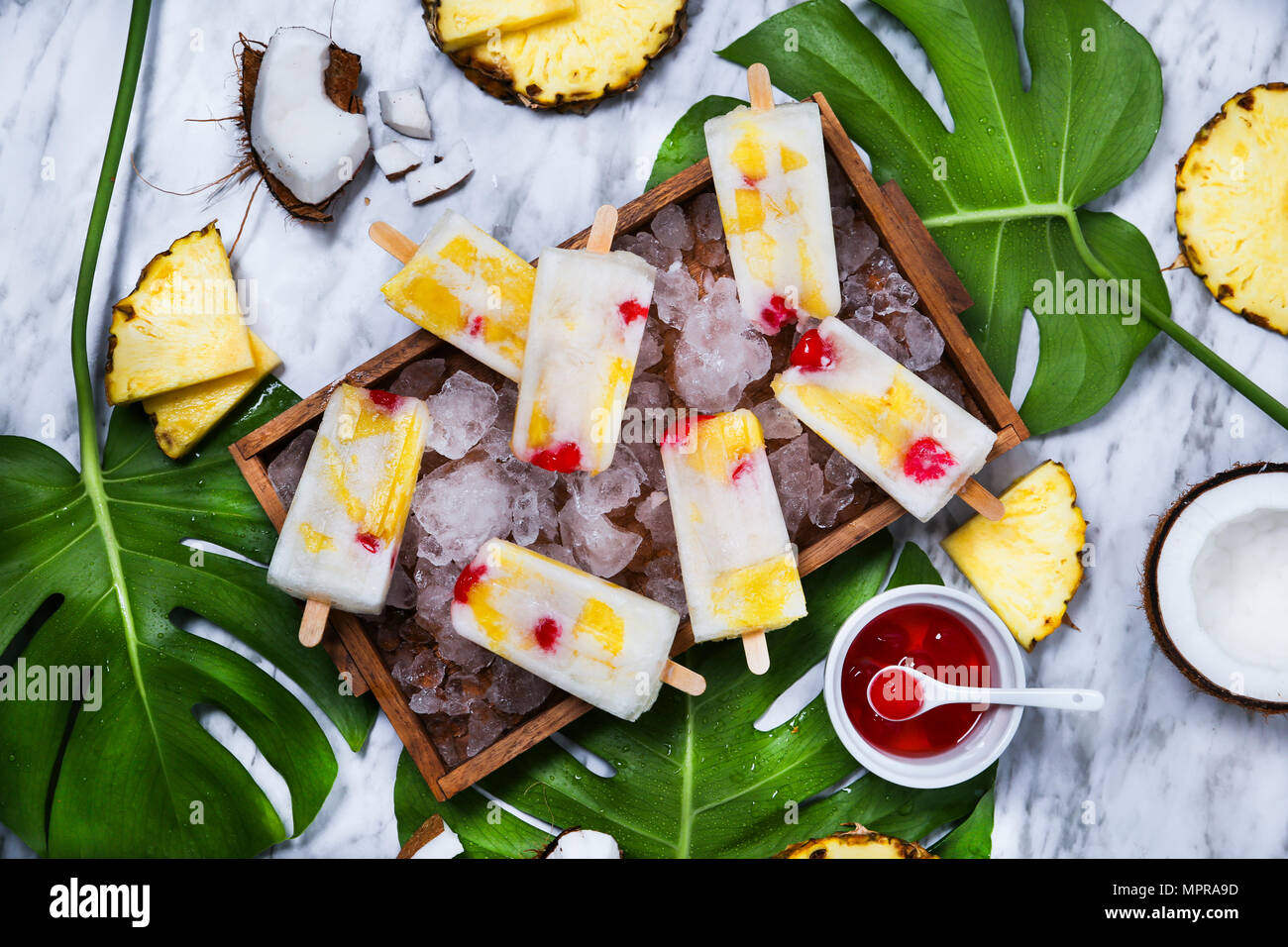 Pina Colada Eis am Stiel mit kandierten Kirschen und Ananas auf Blatt Stockfoto