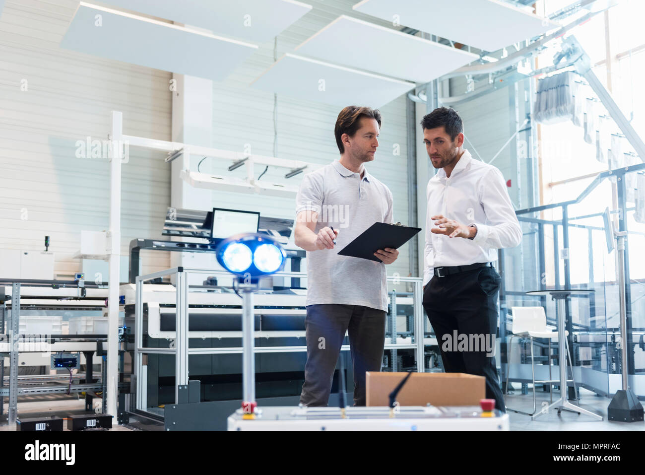 Zwei Männer mit Zwischenablage sprechen in der Factory Stockfoto