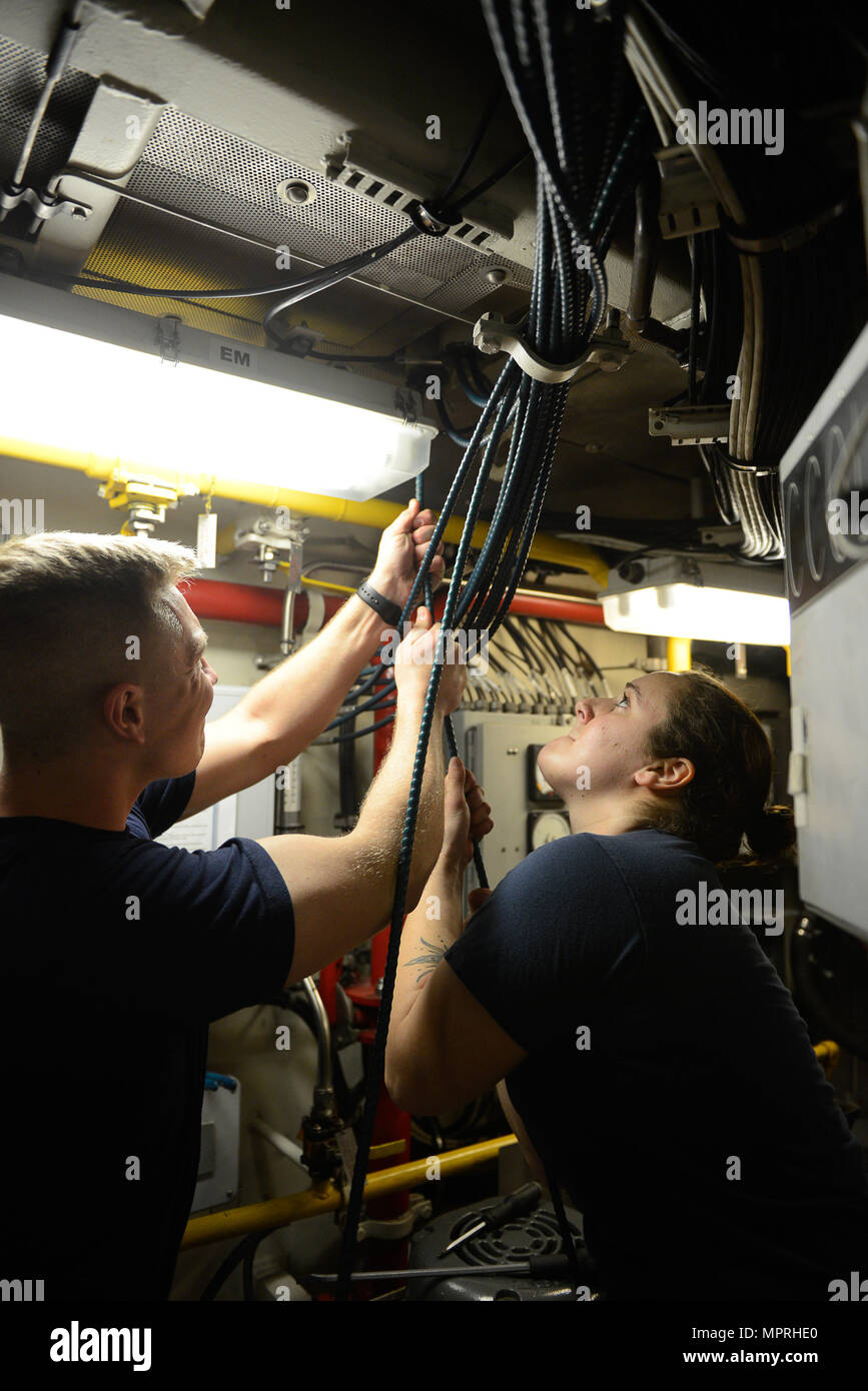 Seaman Jordanien Popovec (Links) und Petty Officer 3rd Class Catherine  Desmarais (rechts) nach unten ziehen, um den Not-Aus-Kabel durch die Decke  im Maschinenraum der Coast Guard Cutter Tiger Shark in Newport am