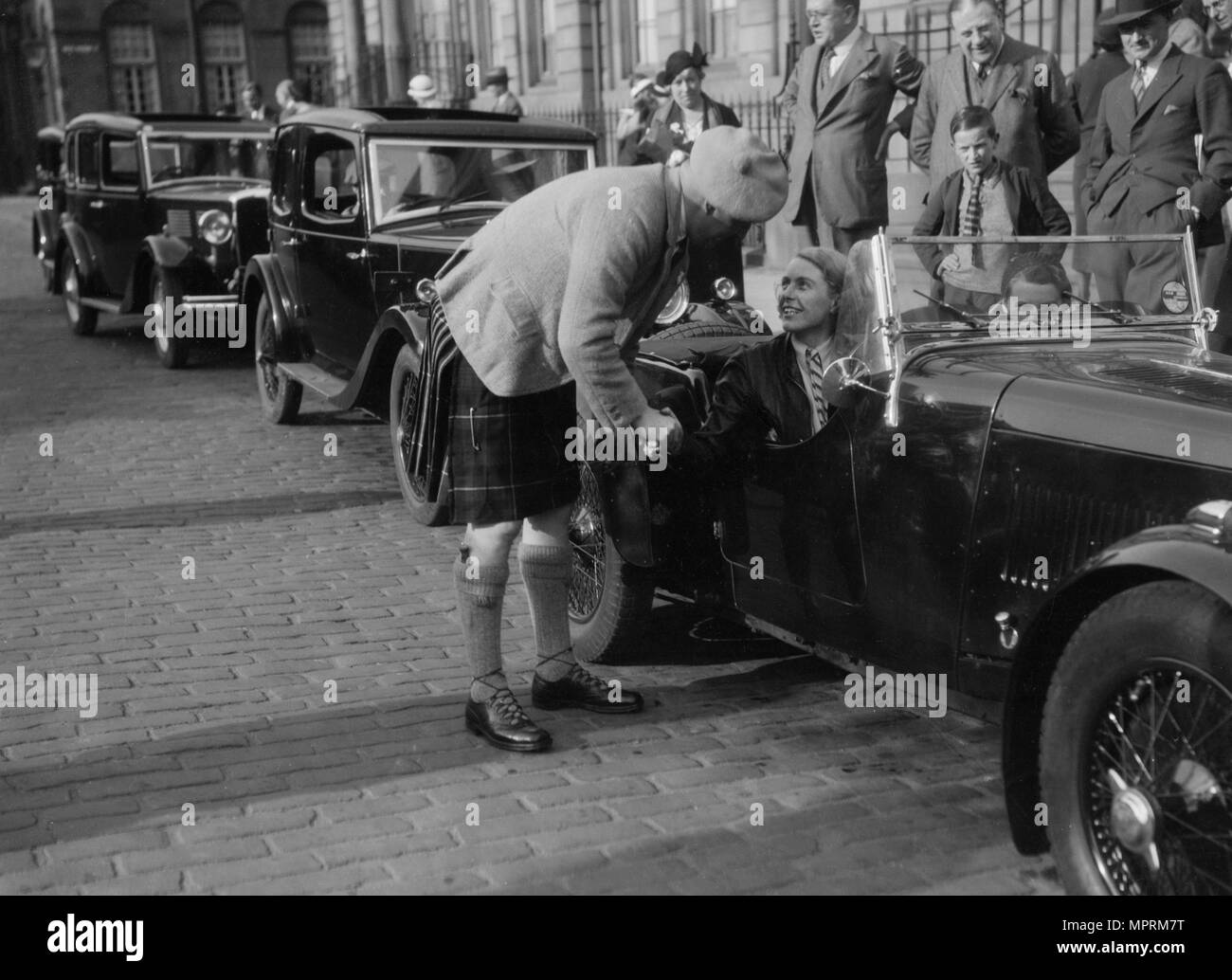 Kitty Brunell in Ihrem Aston Martin, Chatten zu einem Mann in Highland dress, rsac Scottish Rally, 1933. Artist: Bill Brunell. Stockfoto