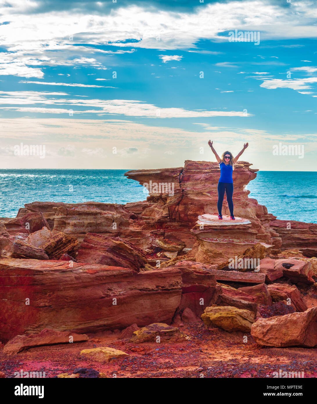 Gantheaume Point, Broome, Australien - 1. Februar 2018. Eine junge Frau stellt sich triumphierend die Arme beim Stehen auf den Felsen am Ende der Gantheaume Stockfoto