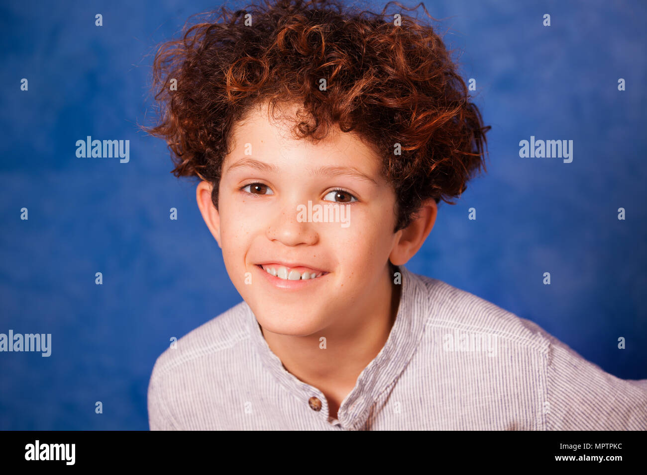 Close-up Portrait von lächelnden Jugendlichen Junge mit lockigem Haar und braune Augen vor blauem Hintergrund Stockfoto