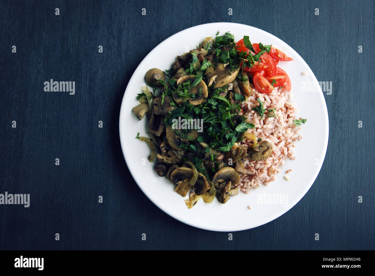 Roter Reis mit Pilzen und Tomaten. Vegane Gerichte. Europäische Küche. Einfach gesundes Mittagessen auf dem schwarzen Hintergrund. Vegetarisches Reisgericht auf dem w Stockfoto