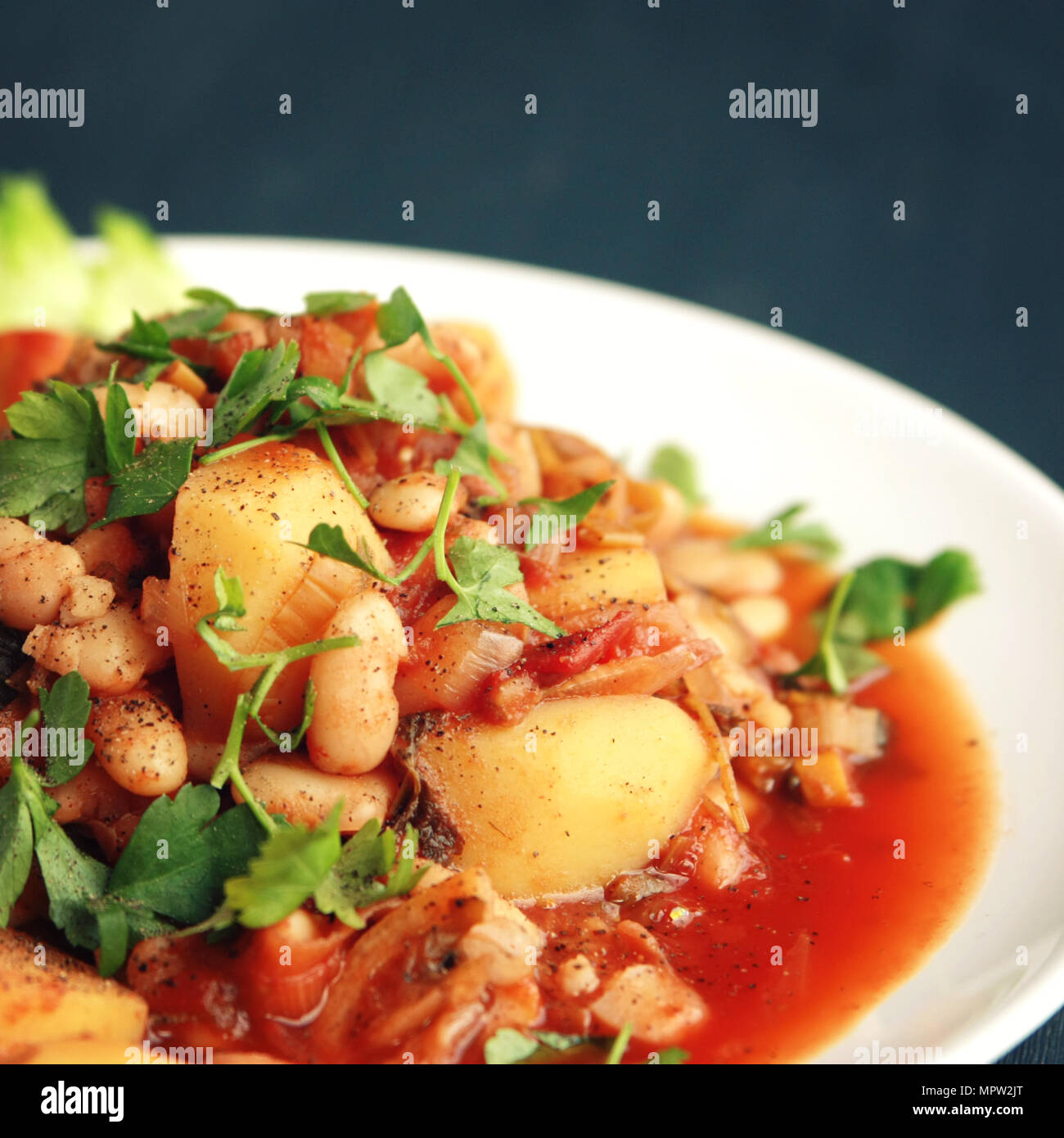 Gemüse Eintopf mit Kartoffeln, weiße Bohnen und Tomaten garniert mit Petersilie. Europäische Küche. Gesund vegan Mittagessen auf dem weißen Teller. Hauptgericht. Veg Stockfoto