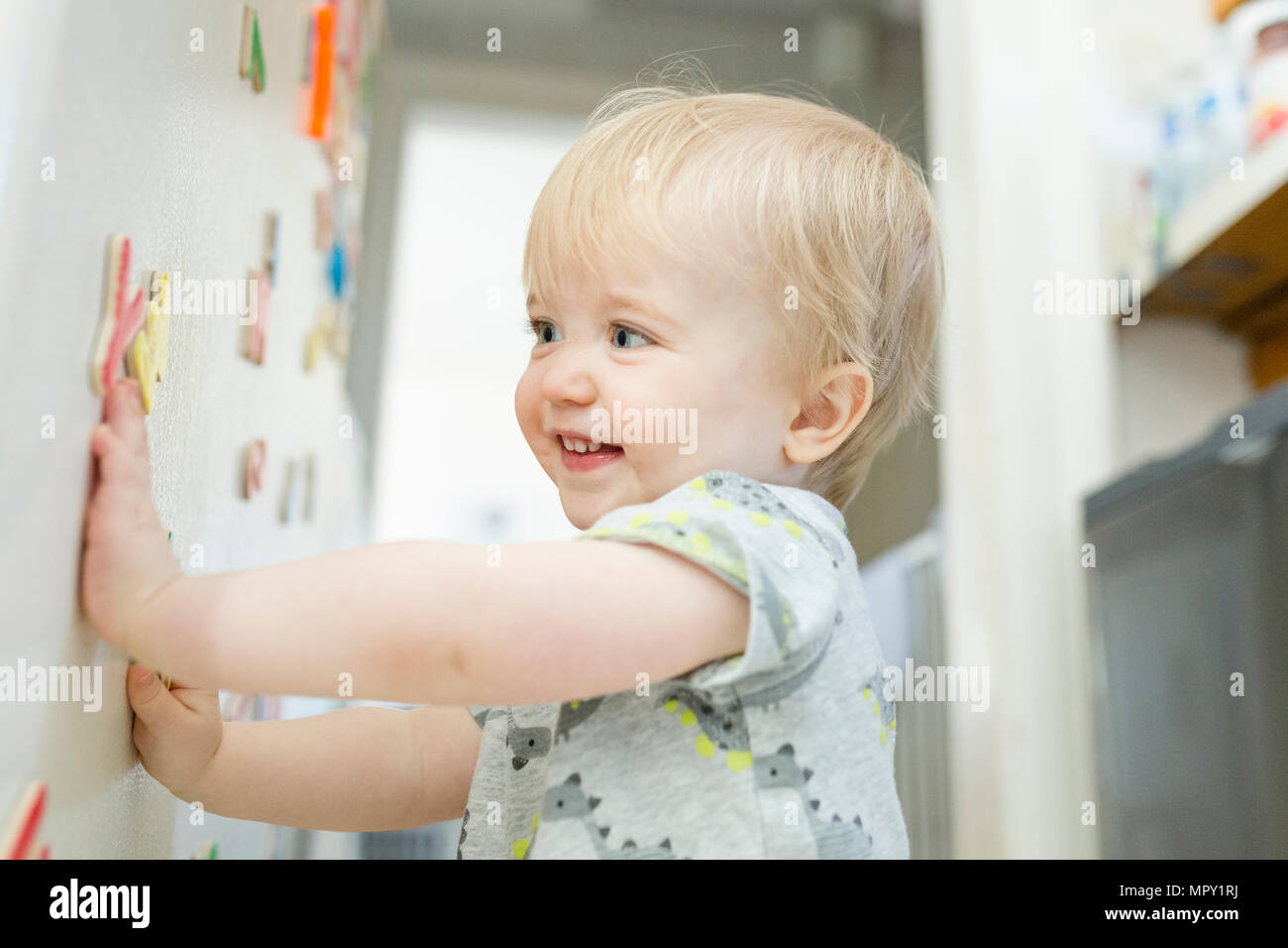 Smiling baby Junge spielt mit bunten magnetische Buchstaben auf metallischen Schaltschrank zu Hause Stockfoto