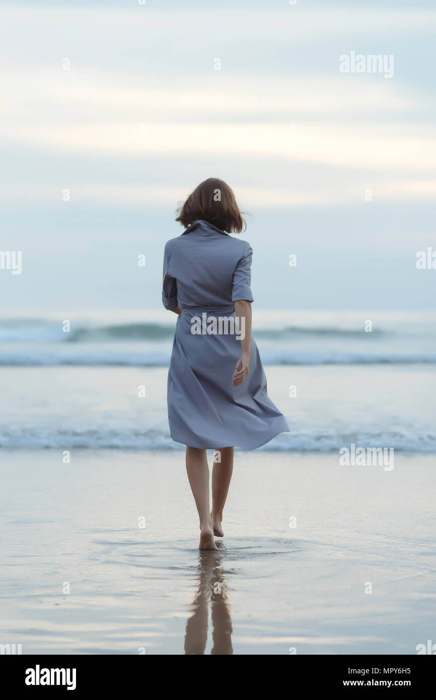 Ansicht der Rückseite des unbeschwerten Frau zu Fuß in Richtung Meer an der Küste am Strand bei Sonnenuntergang Stockfoto