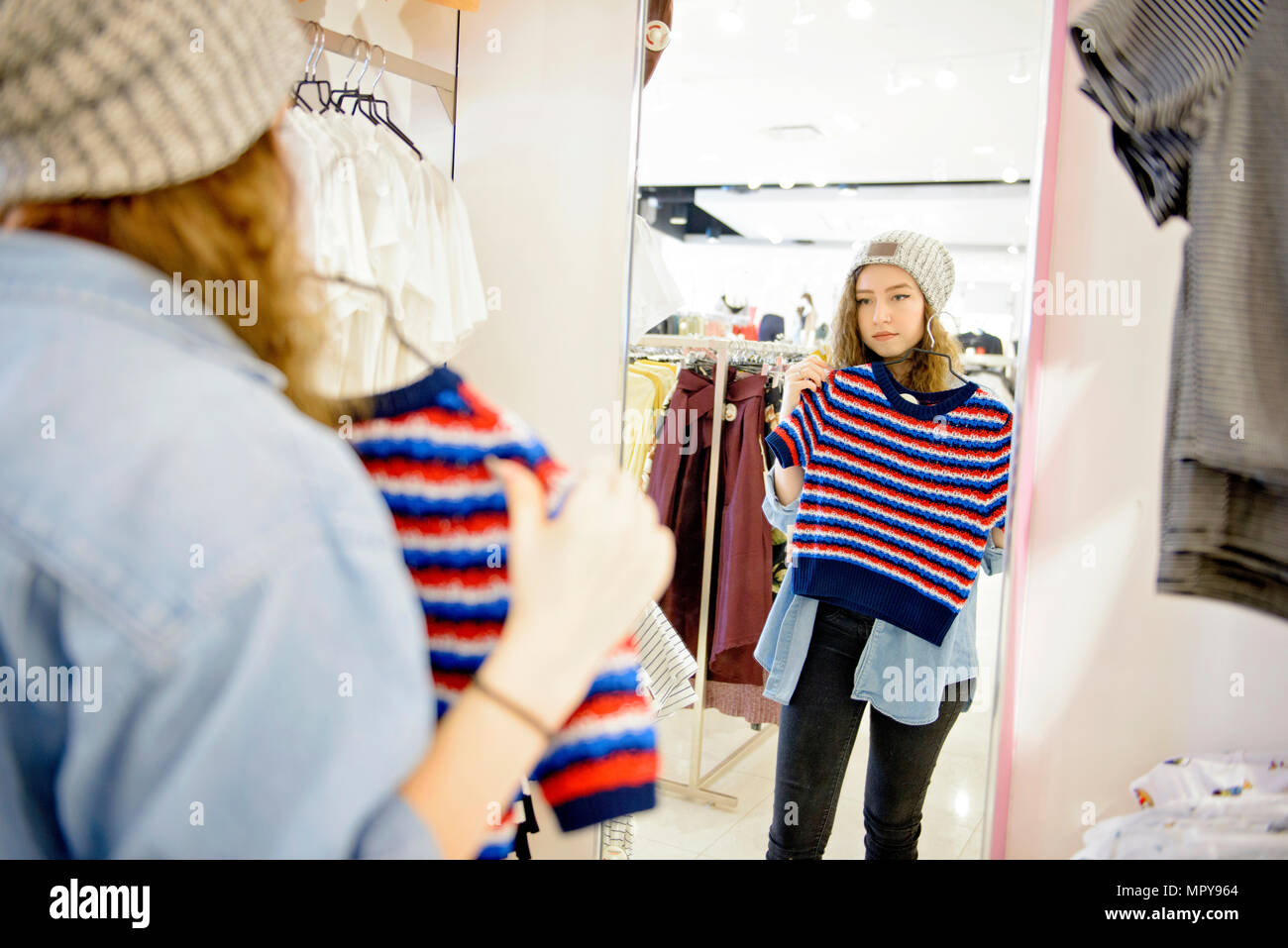 Junge Frau mit Kleidung vor dem Spiegel beim Einkaufen bei Store Stockfoto