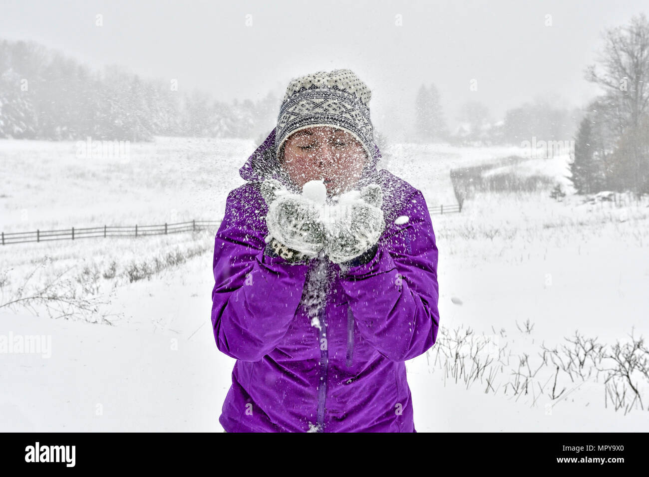 Frau Schneegestöber beim Stehen auf Feld bei Schneefall Stockfoto