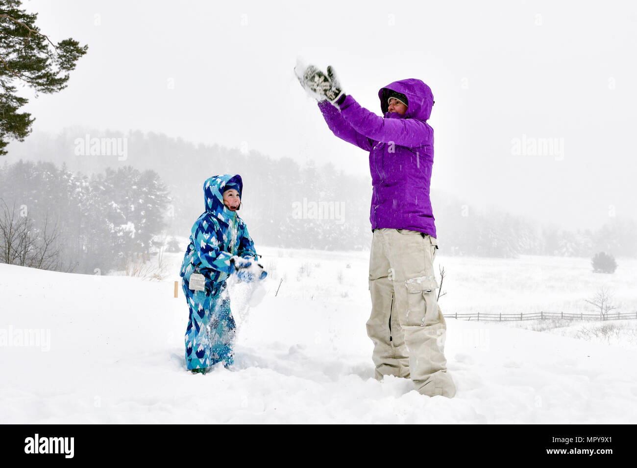 Mutter und Tochter spielen mit Schnee beim Stehen auf gegen den Himmel Stockfoto