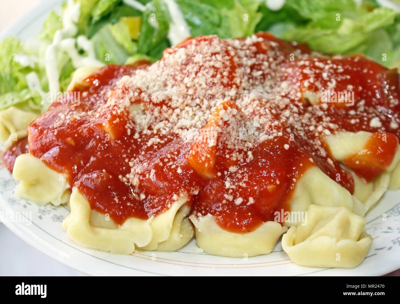 Käse gefüllte Ravioli mit hausgemachter Tomatensoße garniert mit geriebenem Parmesan. Salat mit Dressing cremig auf der Seite Stockfoto