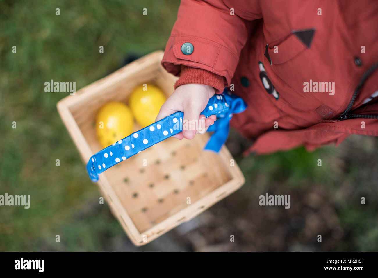 Junge trägt einen roten Mantel mit einem Osterkorb auf eine Ostereiersuche im Garten. Stockfoto