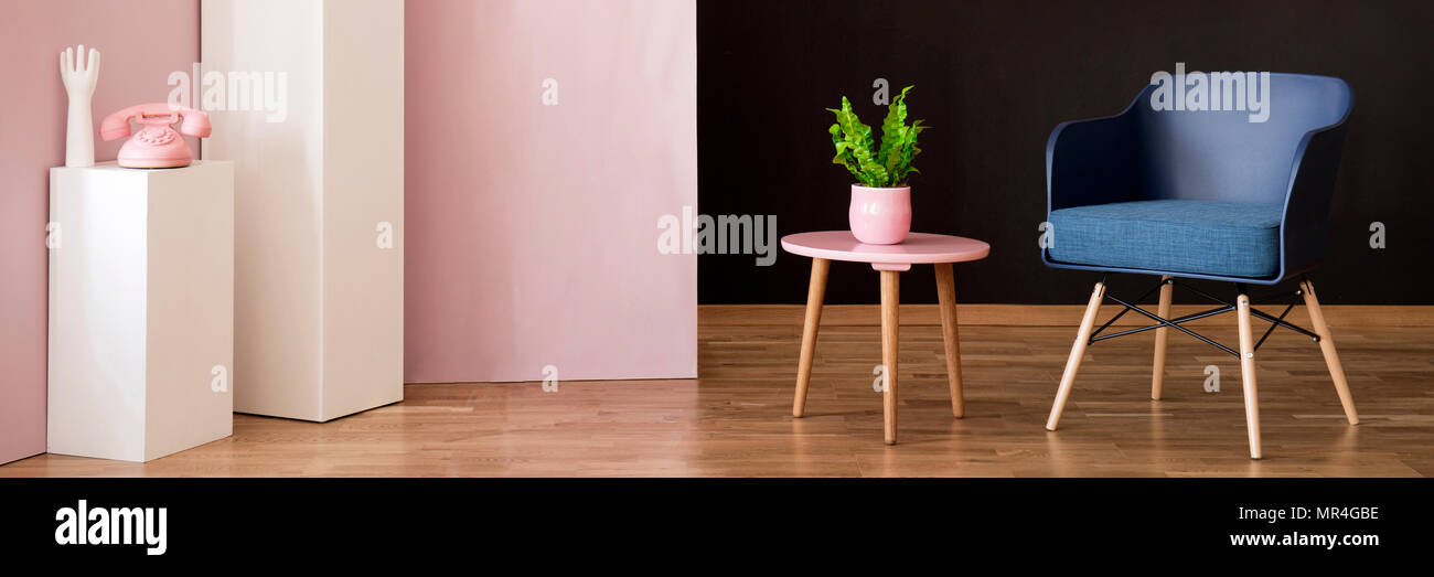 Grüne Pflanze in rosa Topf auf einem hölzernen Ende Tisch neben einem marine blau Sessel in dunklen Inneneinrichtung Stockfoto