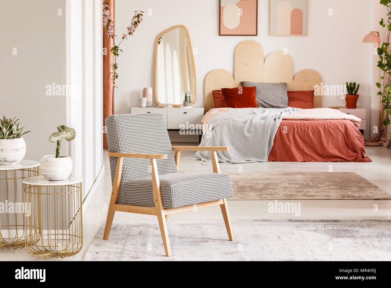Gemusterte hölzernen Sessel neben Gold Tabelle in orange Schlafzimmer mit Doppelbett. Real Photo Stockfoto