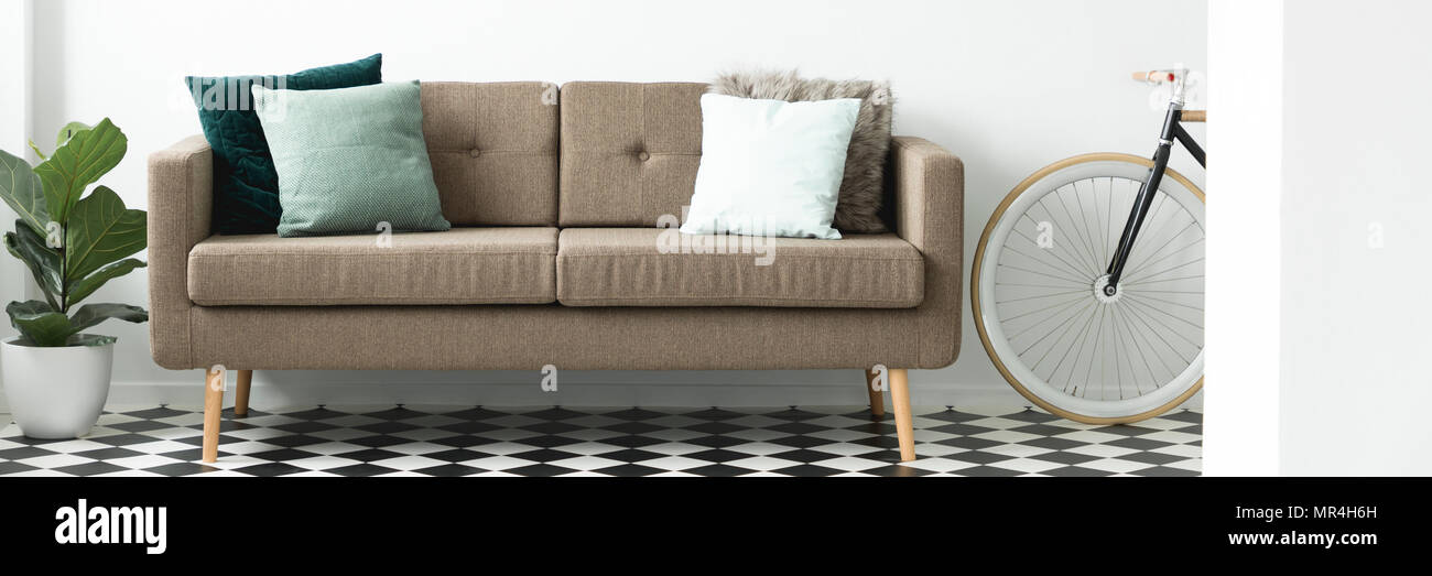 Braun Sofa mit dekorativen Kissen in Weiß Wohnzimmer Interieur mit Linoleum Boden gelegt, Frische Pflanzen- und Bike Stockfoto