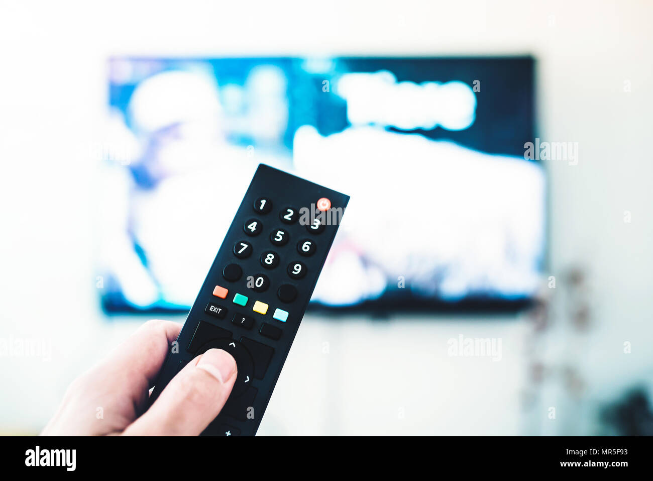 Person mittels Fernbedienung gegen TV auf weiße Wand Stockfoto