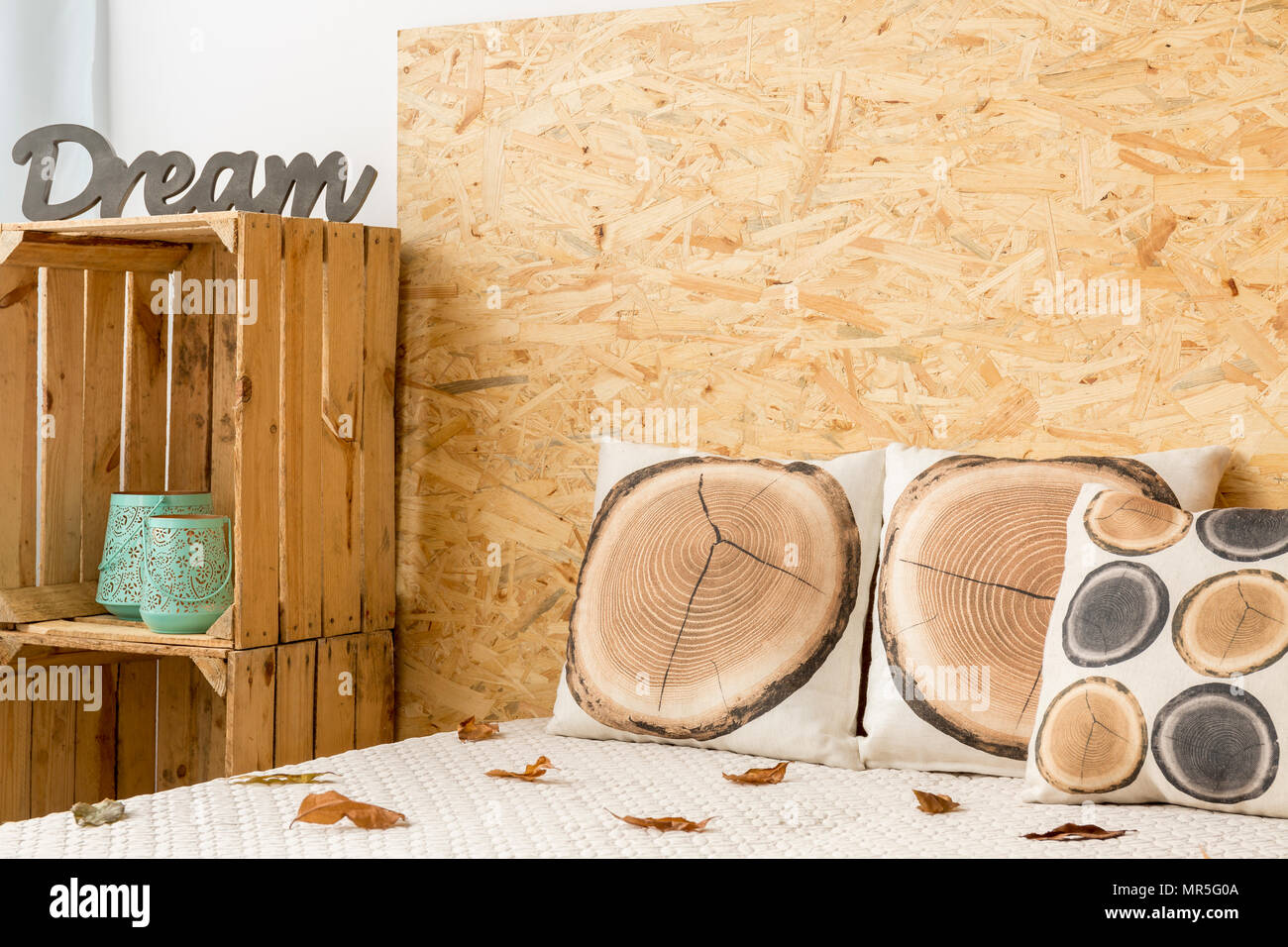 Komfortables Bett mit Natur themed Kissen und Blätter auf Bettwäsche und Holzkisten Stockfoto