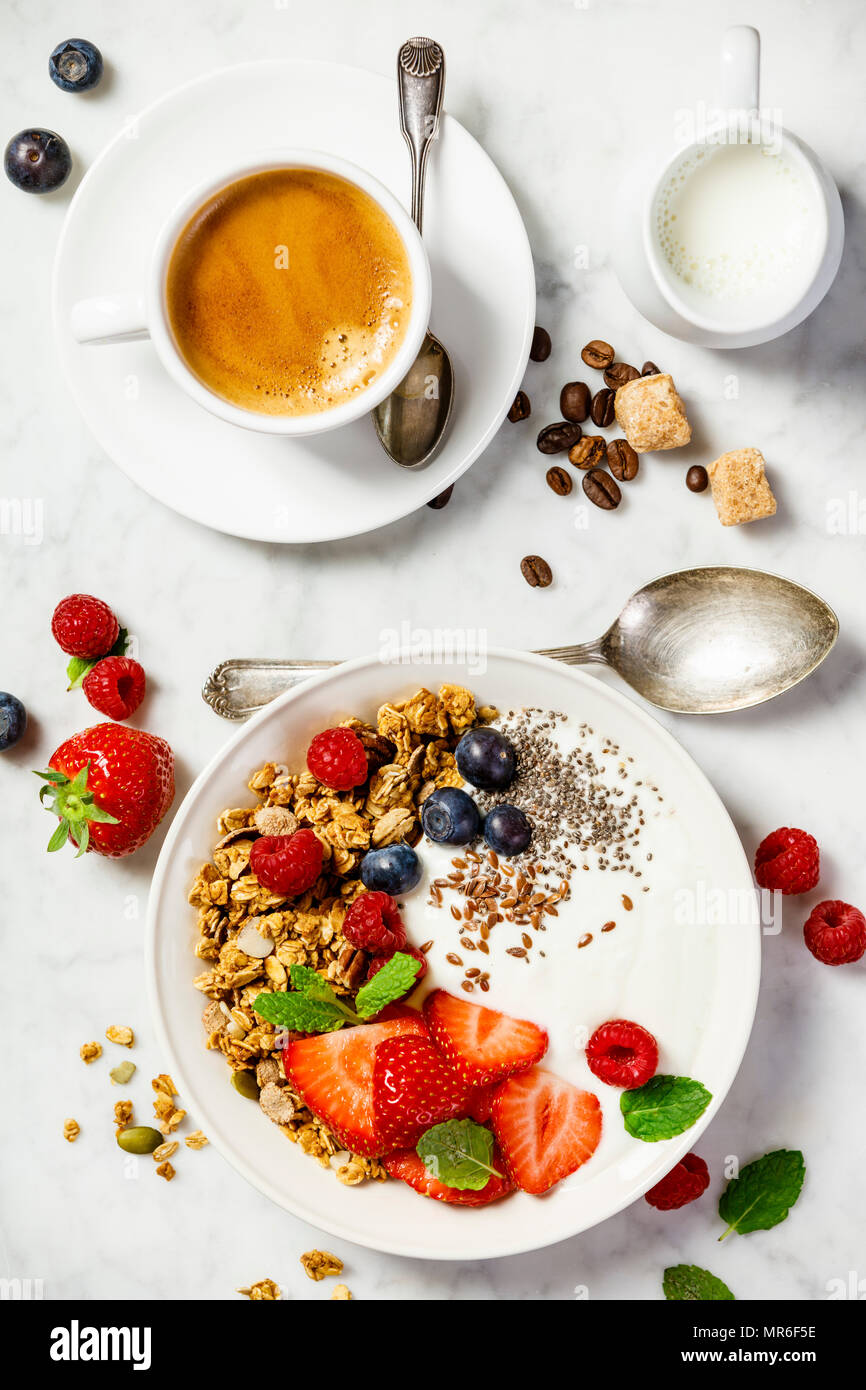 Gesundes Frühstück mit Kaffee und einer Schale mit hausgemachtem Müsli mit Joghurt und frischen Beeren auf weißem Hintergrund. Ansicht von oben, flach Stockfoto