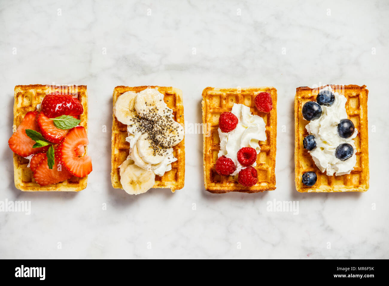 Traditionelle belgische Waffeln mit Schlagsahne und frischen Früchten und Beeren auf weißem Hintergrund. Flach, Ansicht von oben Stockfoto
