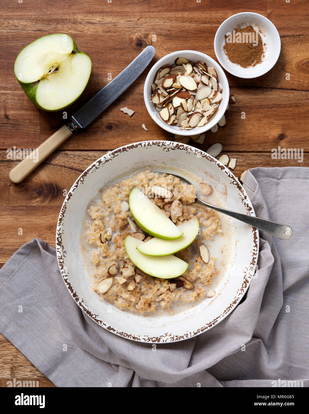 Eine Schüssel mit traditionellen Haferflocken Porridge mit in Scheiben geschnittenen Äpfel, gehobelten Mandeln und Zimt gegen einen hölzernen Hintergrund. Stockfoto