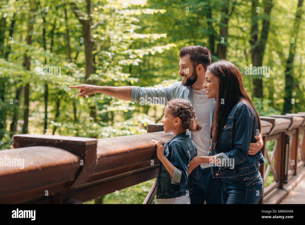 Junge lächelnde interracial Familie stehen auf hölzernen Brücke, während Vater irgendwo in den Wald zeigen Stockfoto