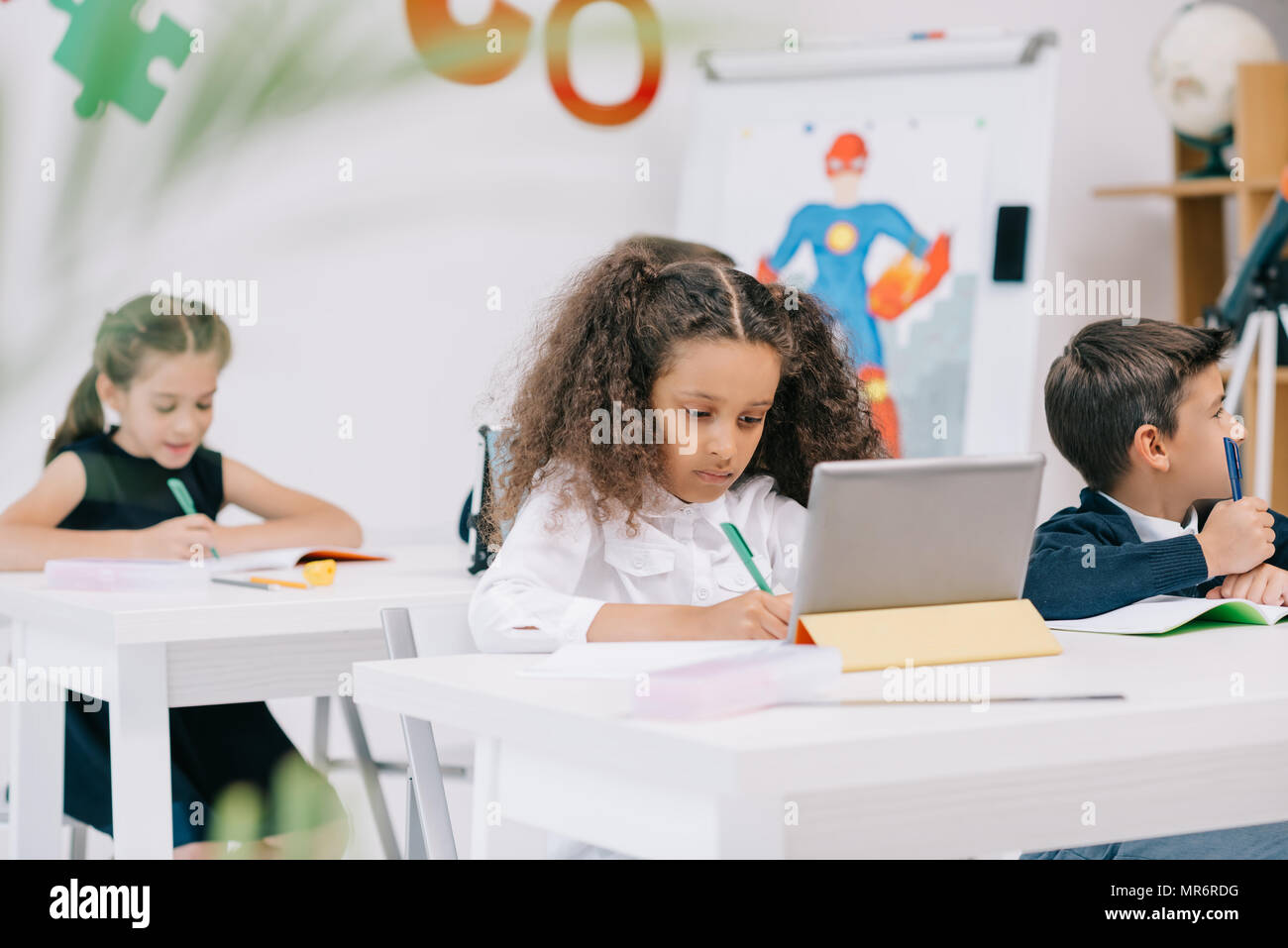 Cute konzentriert multiethnischen schoolkids Studieren mit Übung Bücher und digitale Tablet in der Klasse Stockfoto