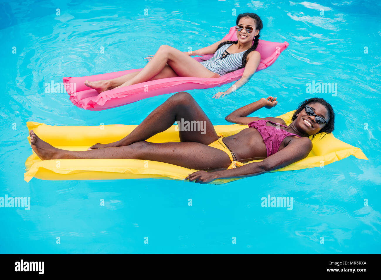 Jungen multiethnischen Frauen schwimmen auf Luftmatratzen im Pool im Resort Stockfoto