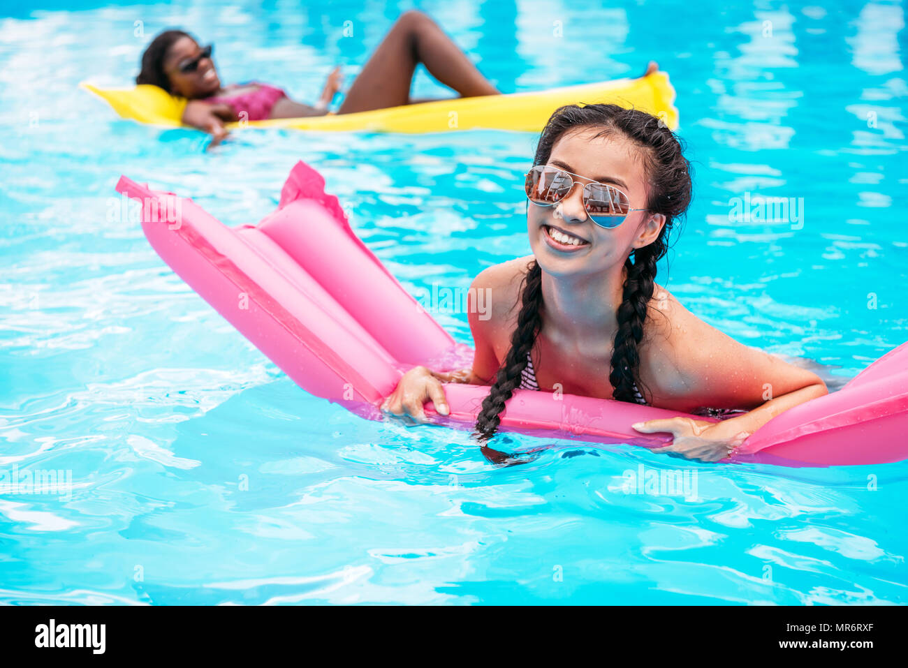 Jungen multiethnischen Frauen schwimmen auf Luftmatratzen im Pool im Resort Stockfoto