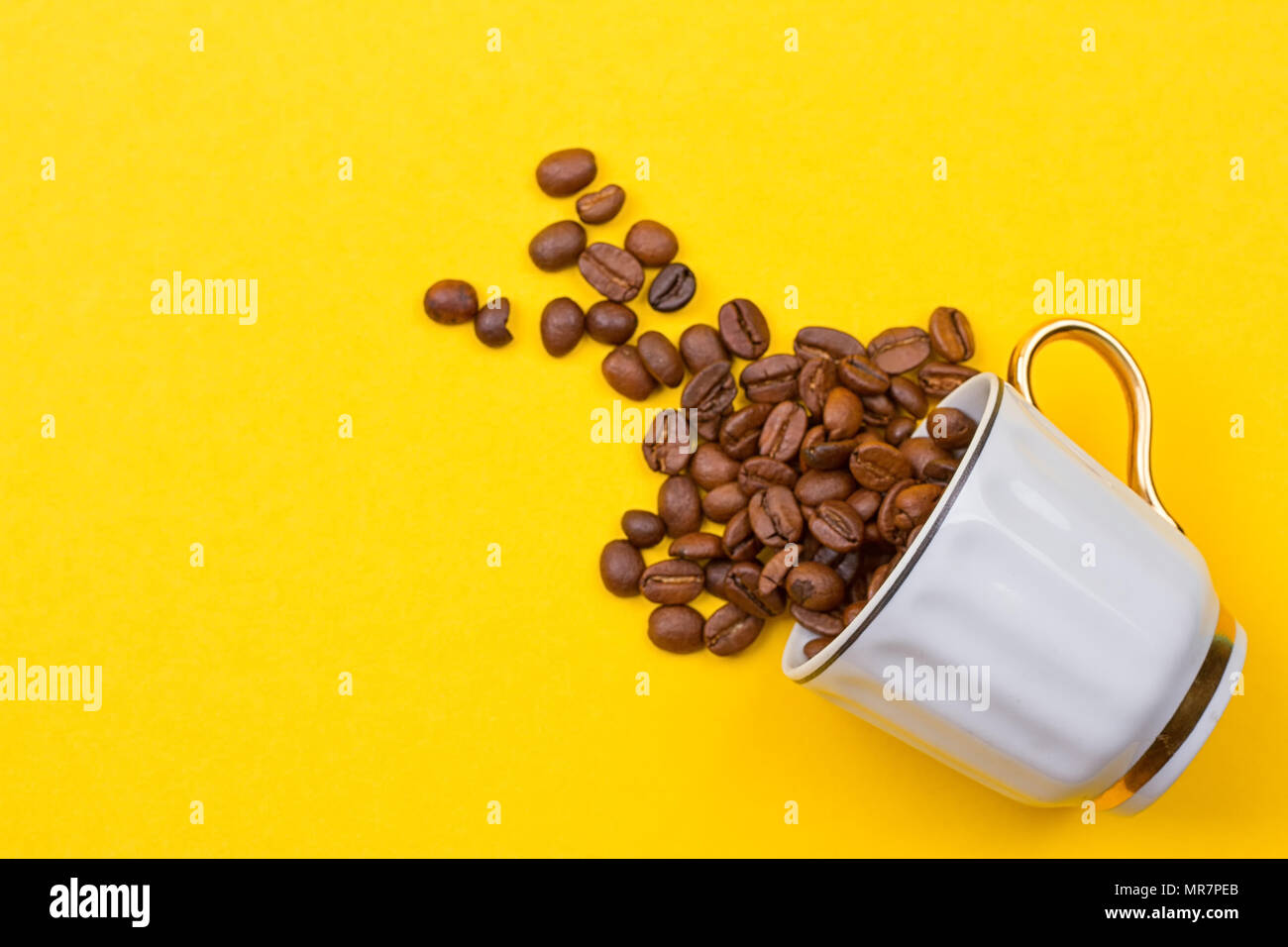 Verschüttete Kaffeebohnen aus einer Schale auf dem yellowbackground Stockfoto