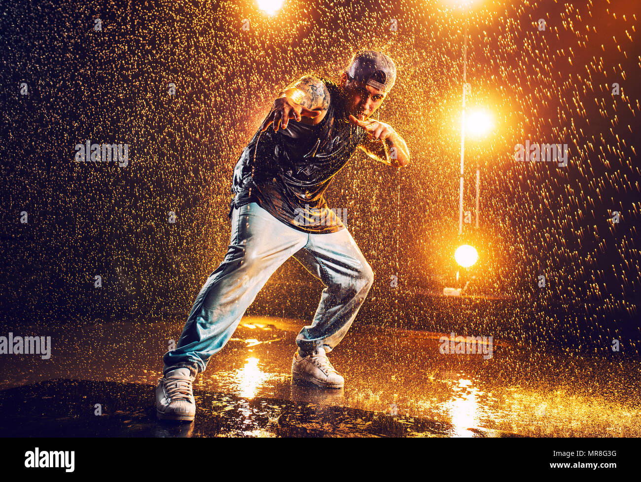 Junger Mann Breakdancer im Club mit Licht und Wasser. Tattoo am Körper. Stockfoto