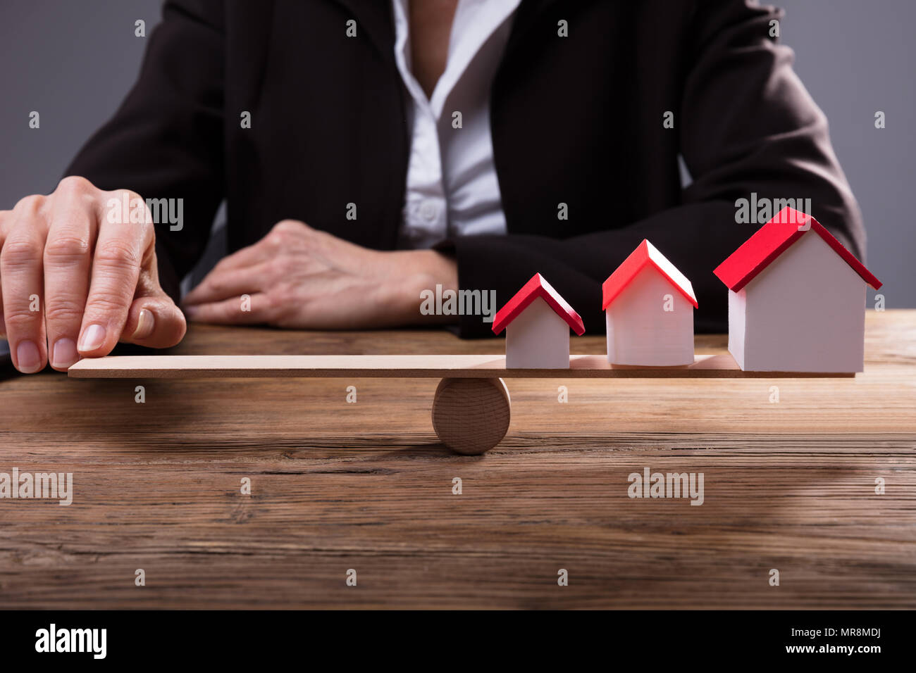 Nahaufnahme eines menschlichen Finger Balancing Haus Modelle auf der Wippe über Holz- Schreibtisch Stockfoto