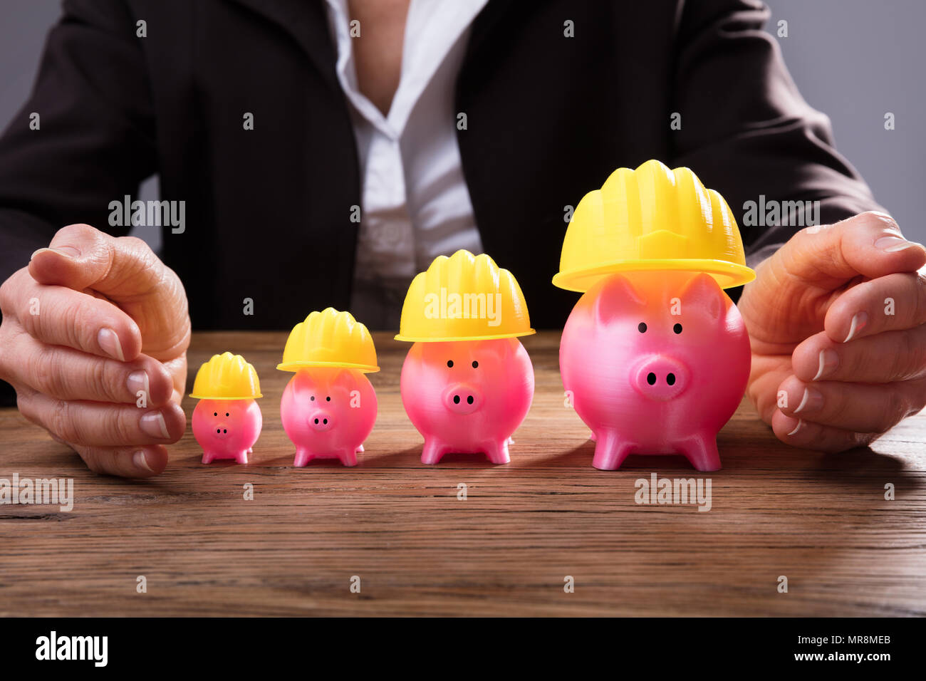 Der Unternehmer schützende Hand steigende Rosa Sparschweine mit gelben Hardhat Stockfoto