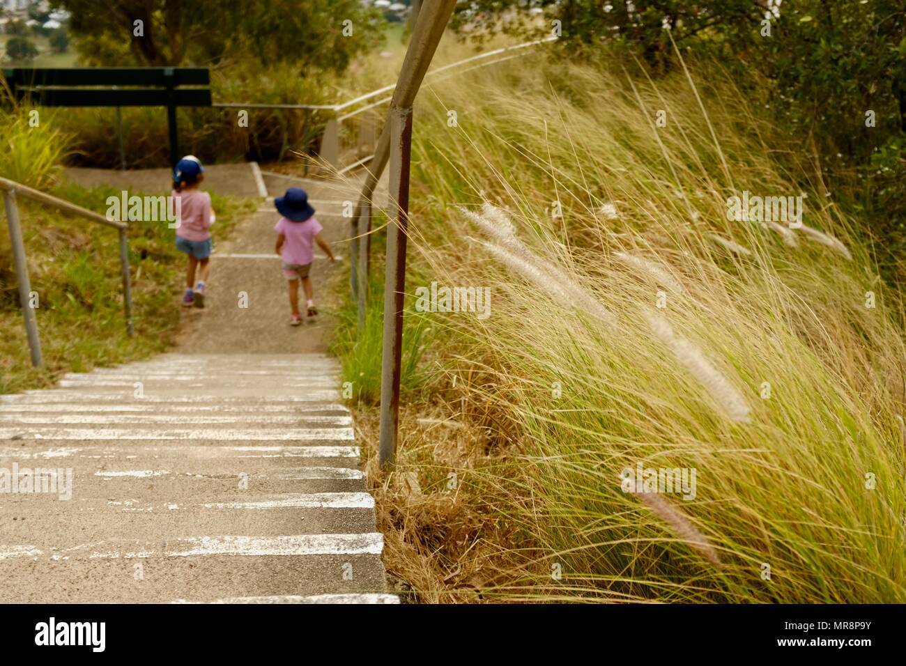 Zwei Kinder an der Unterseite einer Treppe durch langes Gras umgeben, Castle Hill, QLD 4810, Australien Stockfoto