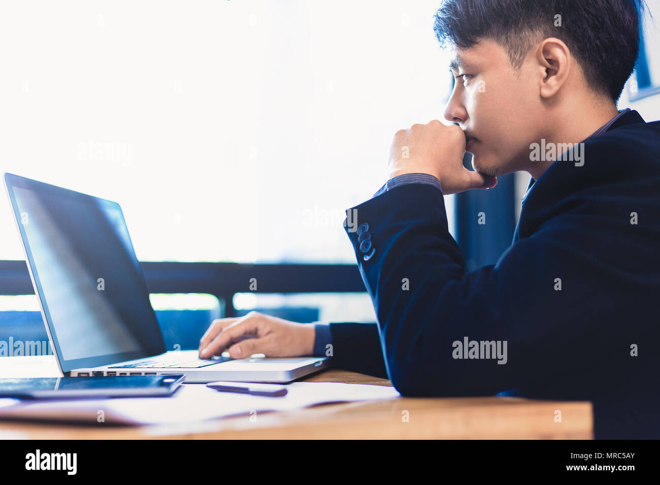 Junge asiatische Geschäftsmann mit der Arbeit an seinem Computer in seinem Büro in der Nähe von große, helle Fenster, selektive Schärfe und Unschärfe Farbe, Tonisierung, gut für Business Theme Stockfoto