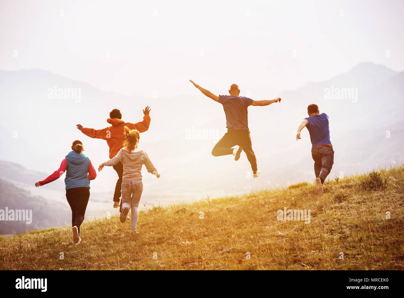 Fünf glückliche Freunde Spaß haben, läuft und springt gegen Sonnenuntergang in den Bergen Stockfoto