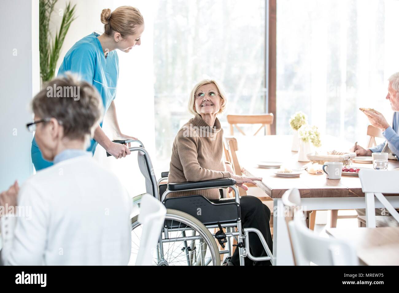 Ältere Frau im Rollstuhl in Richtung care Worker lächelnd. Stockfoto