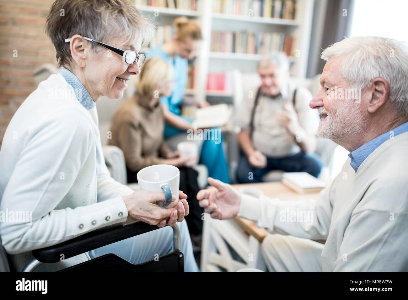 Ältere Frau im Rollstuhl im Gespräch mit männlichen Unhold in Pflege zu Hause. Stockfoto