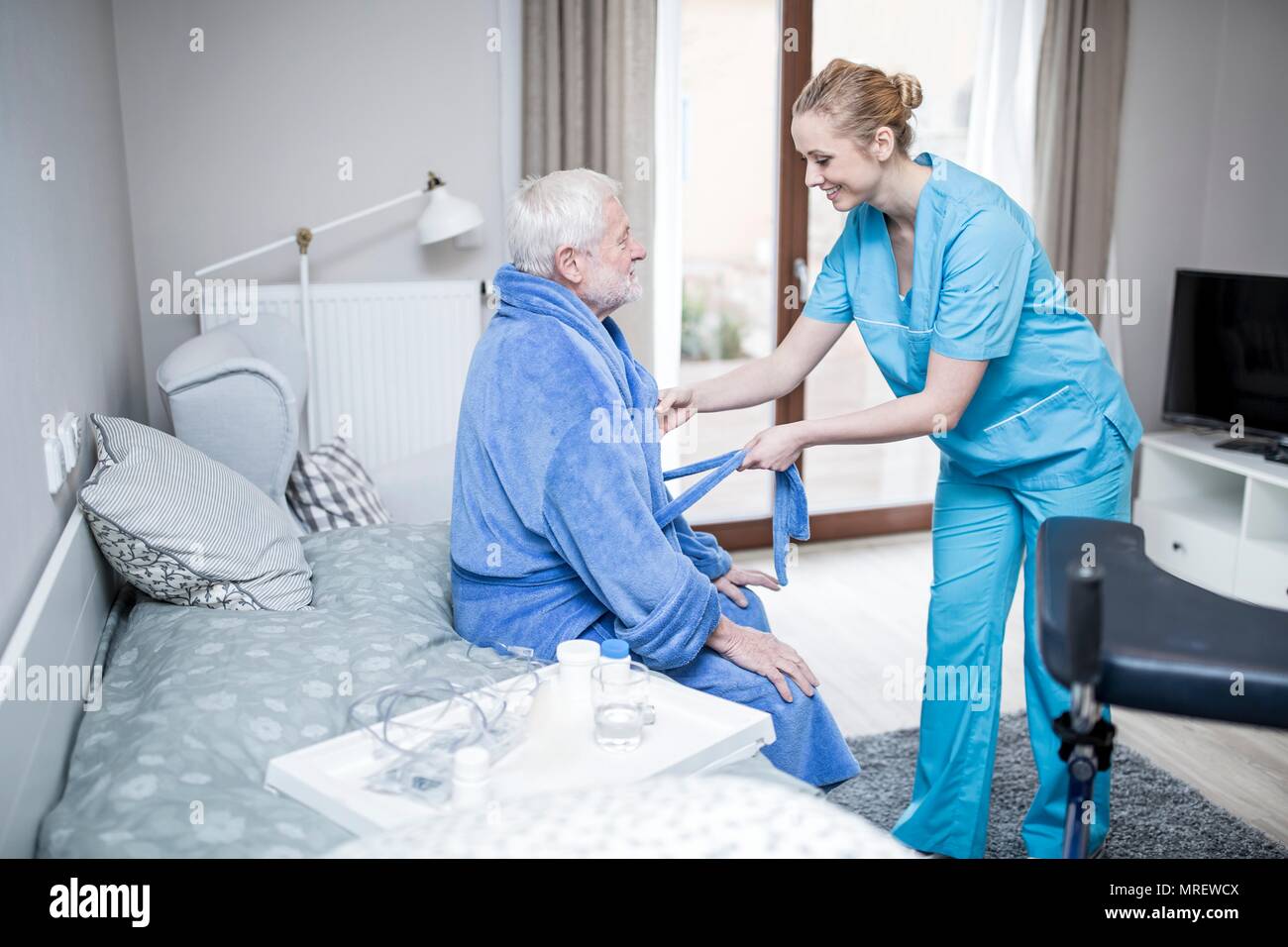 Care worker helfen älteren Menschen auf Morgenmantel zu setzen. Stockfoto