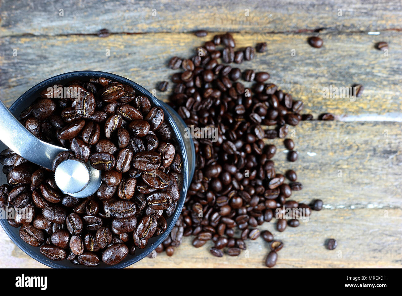 Fokus auf gerösteten Kaffeebohnen in einer kaffeemühle von Hand. Und geröstete Kaffeebohnen auf Holz- Hintergrund. Stockfoto