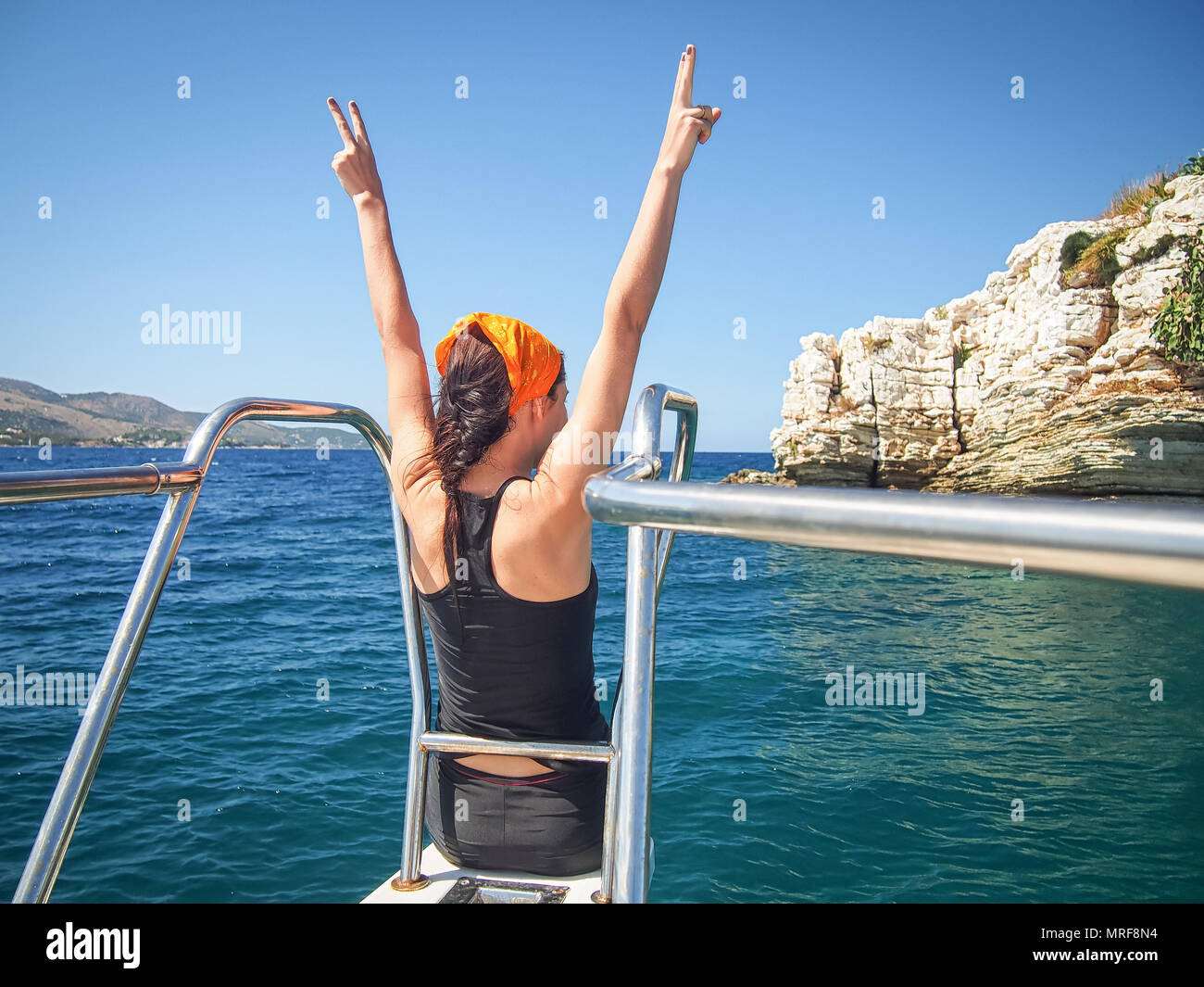 Junge Frau sitzt auf der Nase einer Yacht gegen das Meer zeigt Zeichen der Sieg Stockfoto