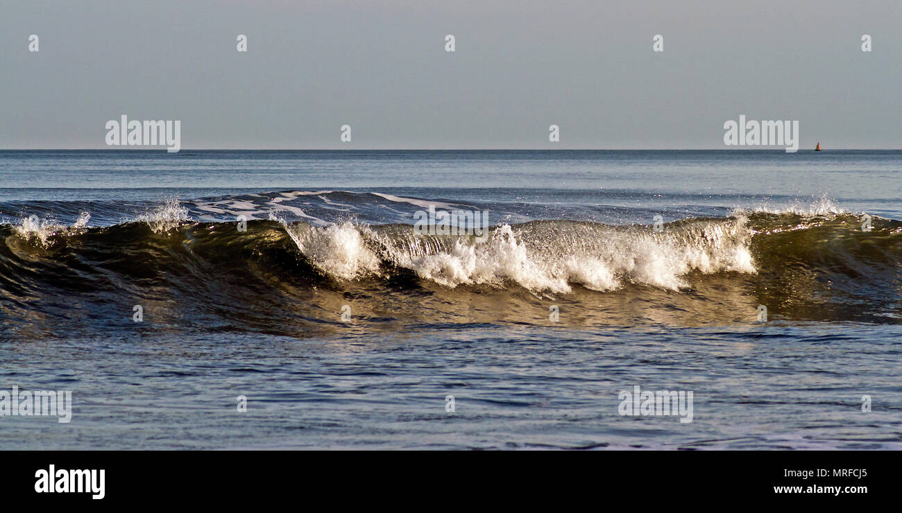 Eine brechende Welle rollt sanft in die seichten Gewässer der Scarborough South Bay. Stockfoto
