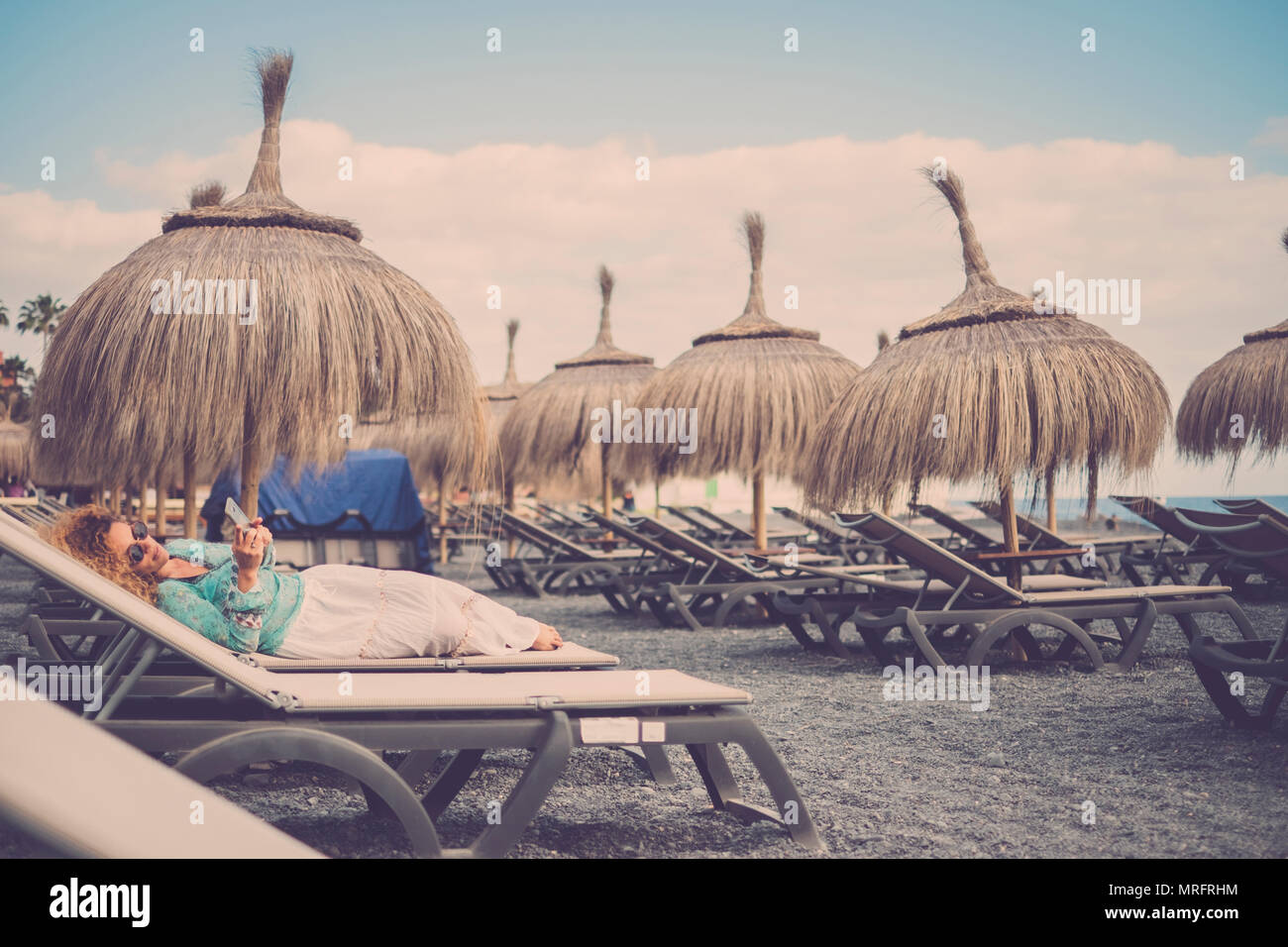 Schönen kaukasischen Frauen mittleren Alters auf die Sitze legen am Strand mit tropischen Sonnenschirme. Reisen und Ferien rest Konzept. Bleiben Sie verbunden wit Stockfoto
