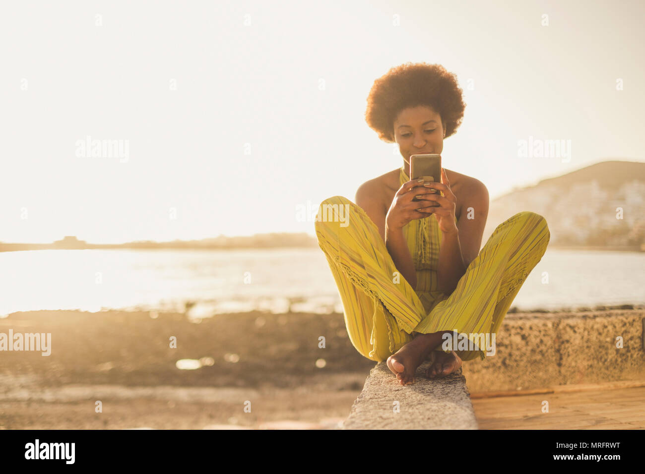 Schönen schwarzen Rasse afrikanische Modell mit schönem Haar mit dem Smartphone sitzen in der Nähe von das Meer und den Strand in Freiheit Freizeit Urlaub Aktivität. conta Stockfoto