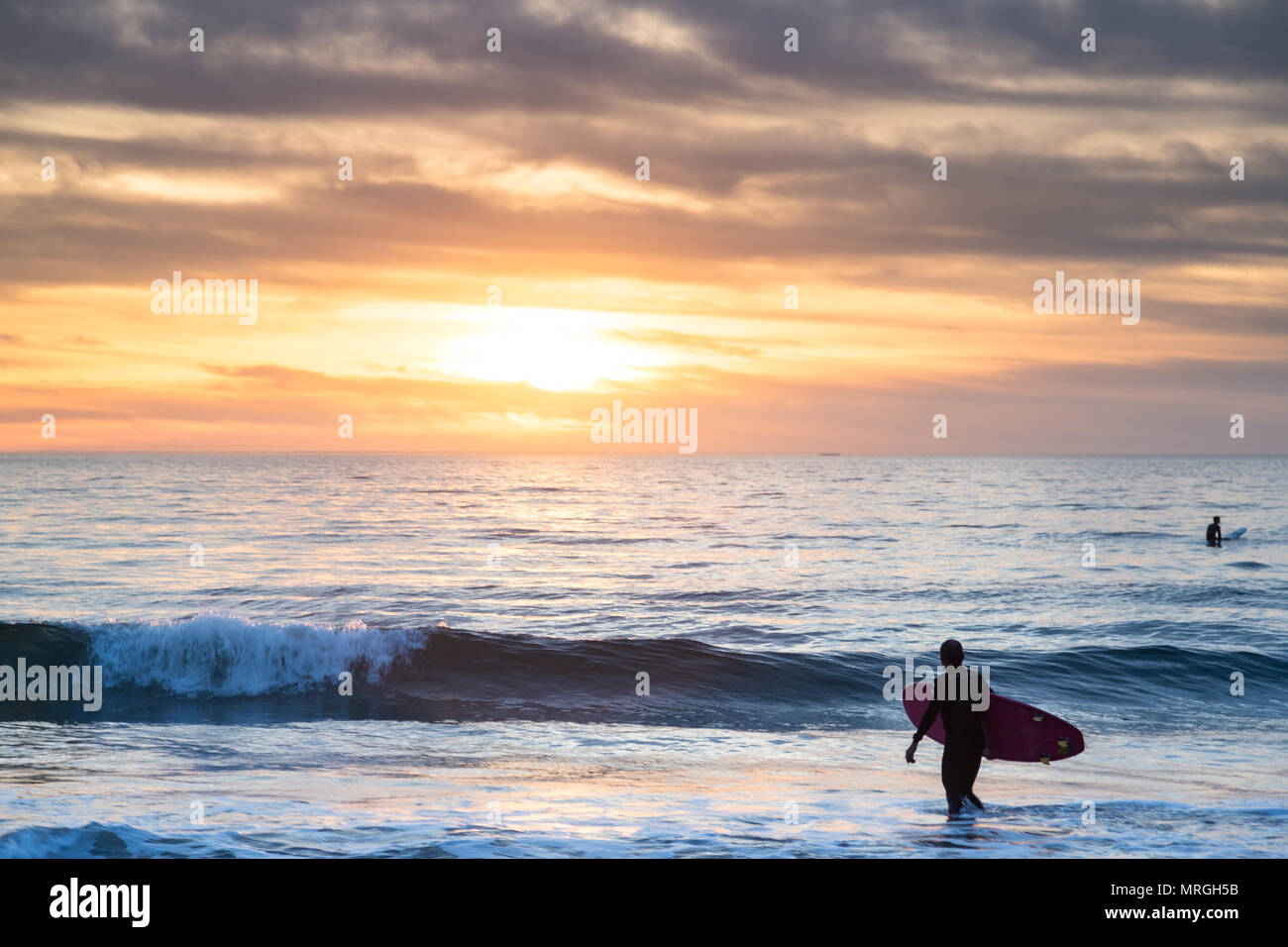 Ein Longboard Surfer Spaziergänge in den Ozean in Manhattan Beach, Kalifornien an einem bewölkten Tag, bereit, ein paar Wellen, bevor es dunkel wird. Stockfoto