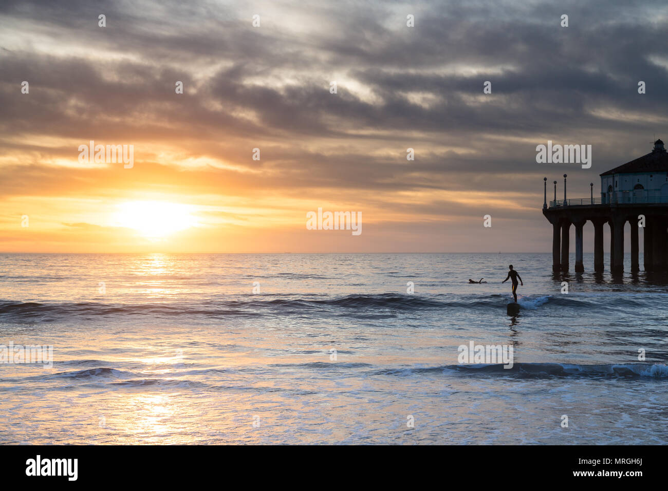 Ein Longboard Surfer Fänge eine letzte Welle neben der Manhattan Beach Pier an einem bewölkten Tag. Stockfoto