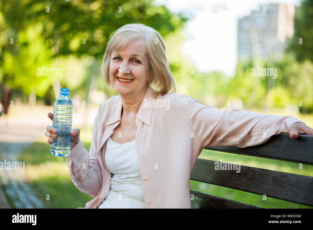 Erwachsene Frau sitzt im Park und Trinkwasser. Stockfoto
