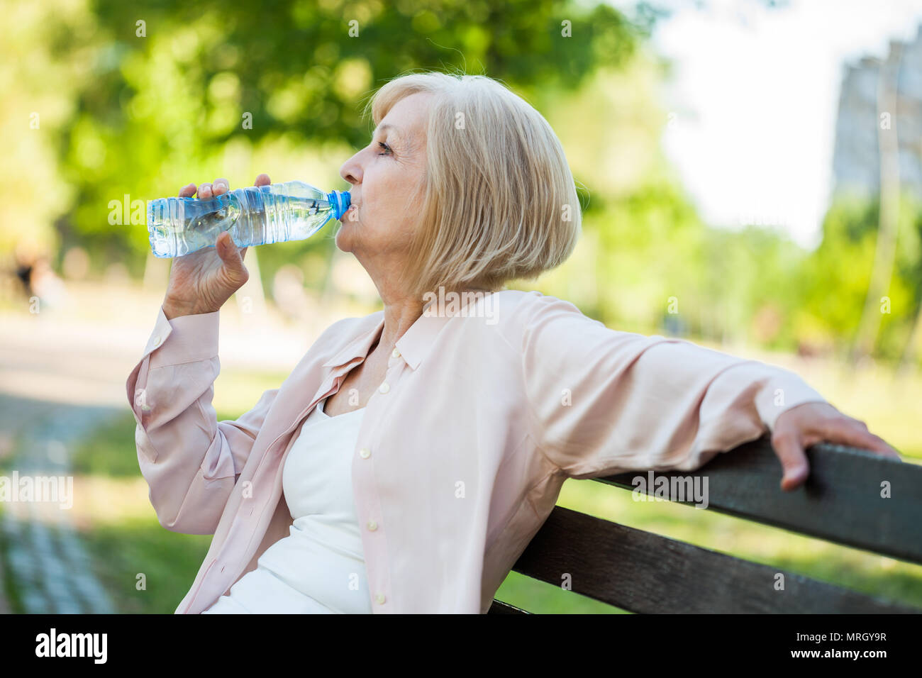 Erwachsene Frau sitzt im Park und Trinkwasser. Stockfoto