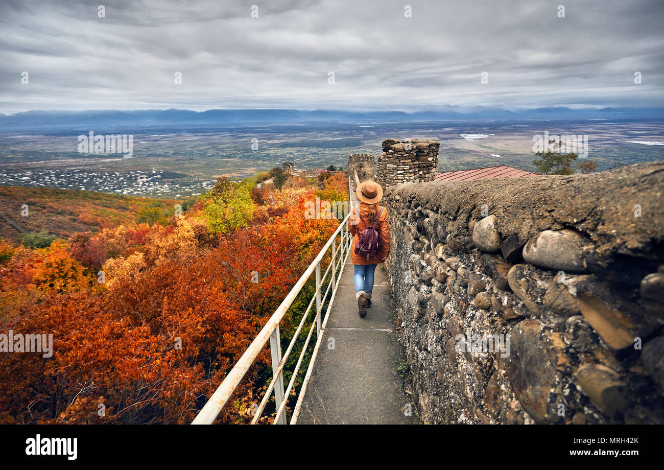 Touristische Frau in braunen Hut und Rucksack zu Fuß auf der alten Stadtmauer mit Blick auf Alasani Valley im Herbst mal in Signagi, Georgien Stockfoto