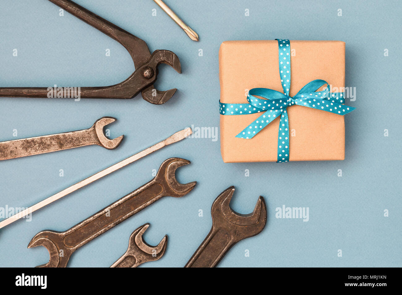 Vatertag Konzept Karte mit Werkzeugen des Menschen auf grauen Hintergrund und Geschenkbox in braunes Packpapier eingewickelt und mit blauer Schleife gebunden. Ansicht von oben. Stockfoto